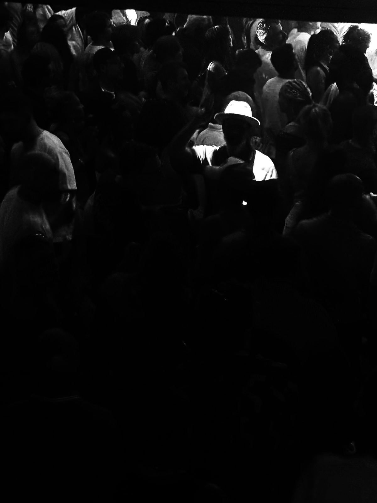 Black-and-white photograph of a crowd in a dim corridor, one figure in a white hat catching the light.