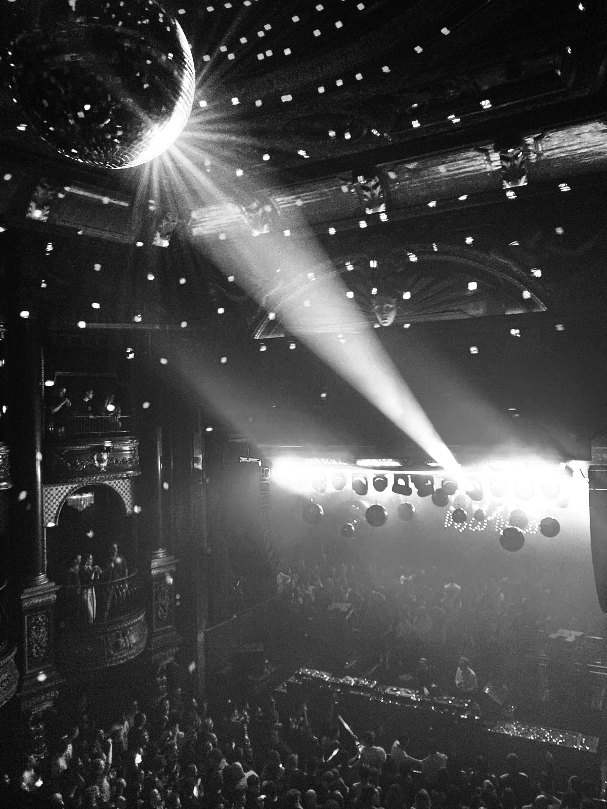 Black-and-white photograph of a mirrorball above a crowded venue, light beams cutting through the dark.