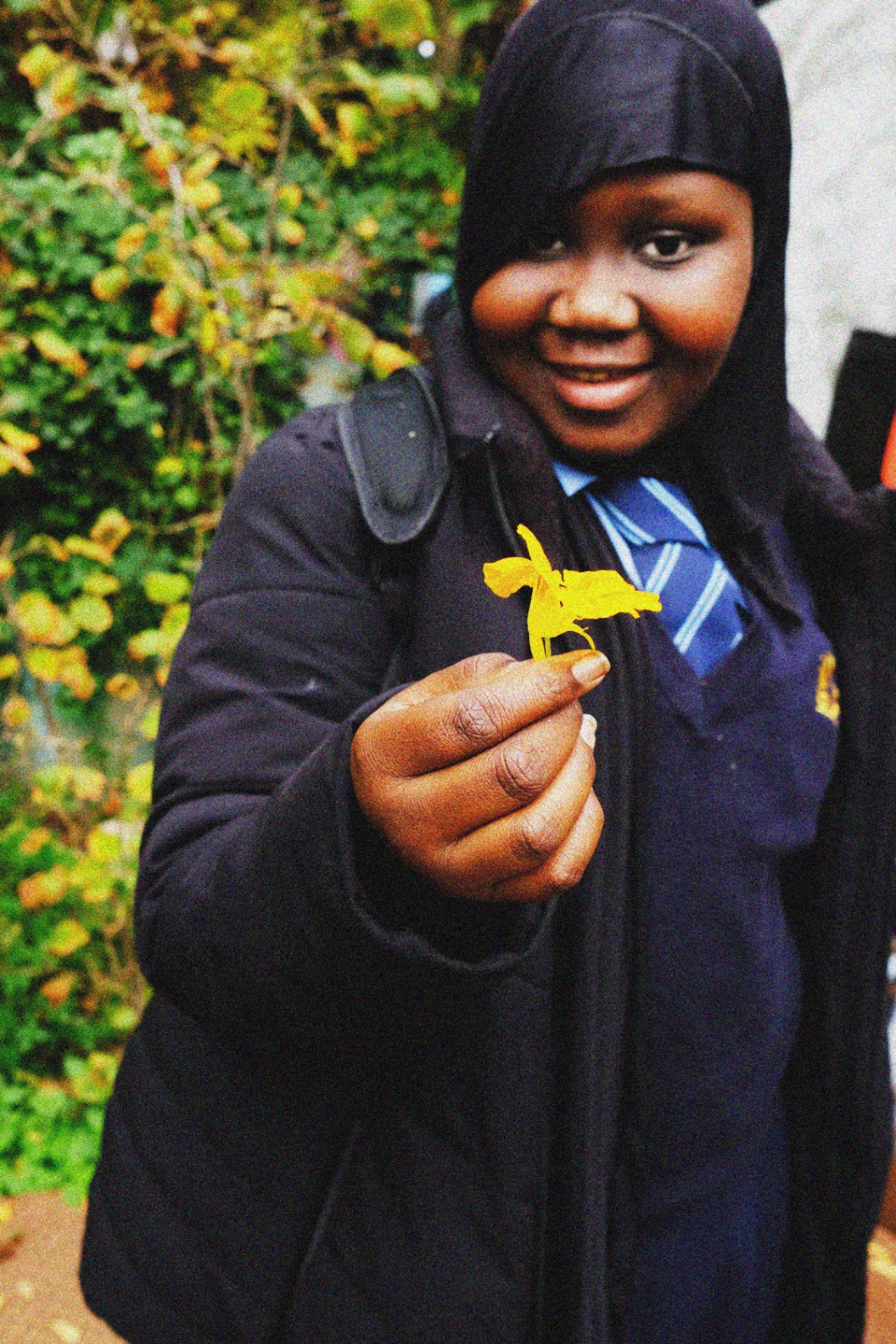 A student smiling and offering a bright yellow daffodil to the camera