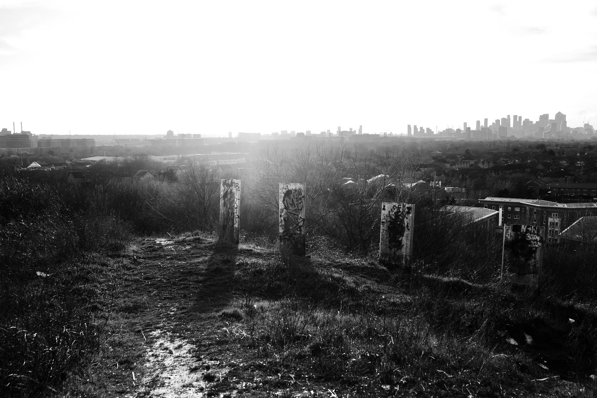 Graffiti-covered concrete posts on top of the Beckton Alps, with the Canary Wharf skyline in the distance.