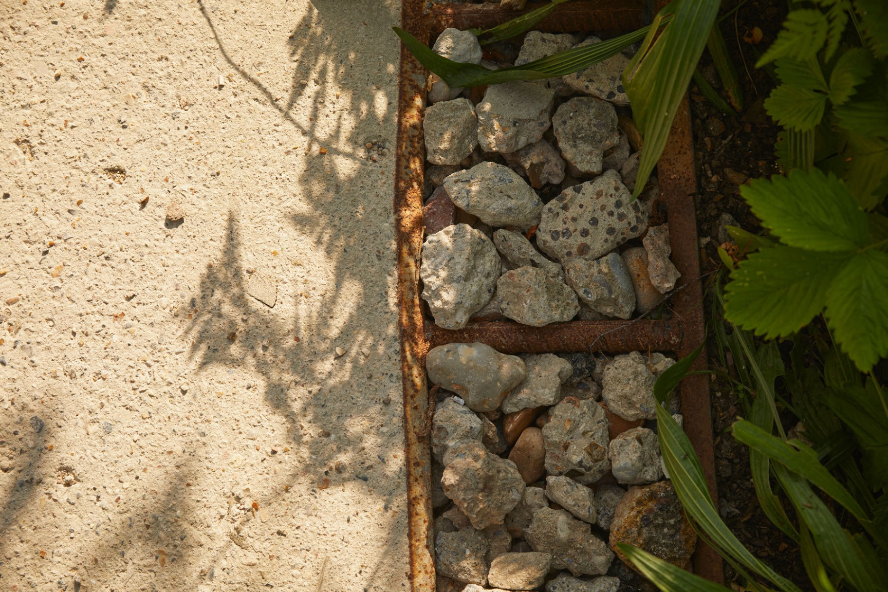 A rusted steel gully filled with crushed stone drainage.