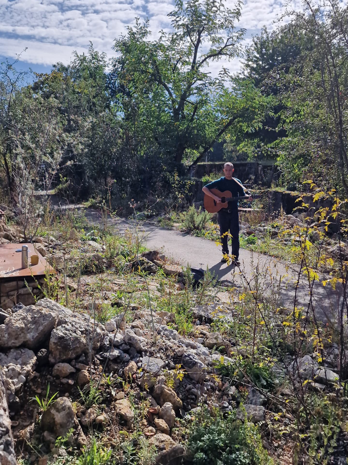 A musician with an acoustic guitar standing on a path in the Markfield Legacy Garden