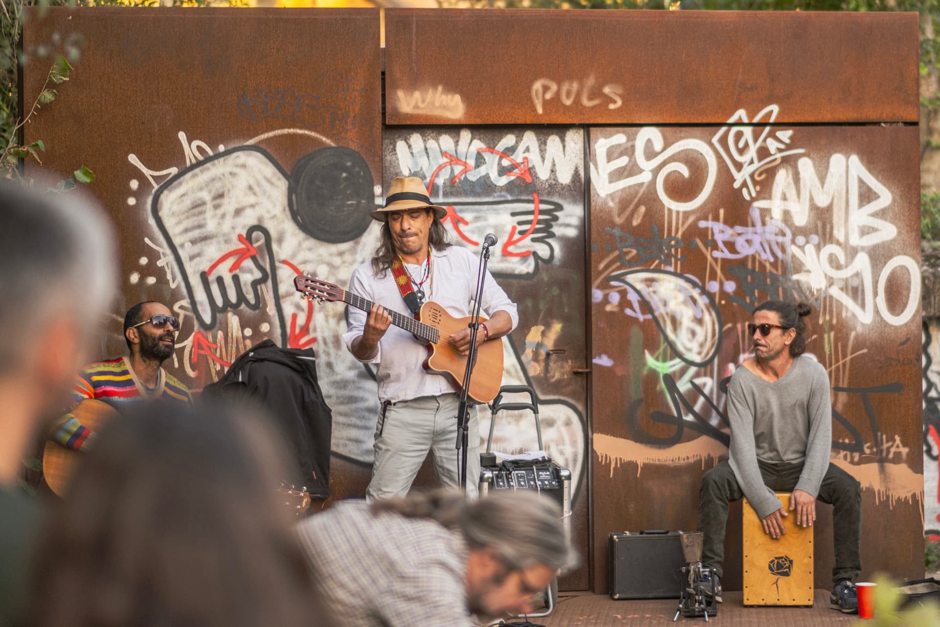 A band playing in front of the graffiti-covered corten shelter in the garden