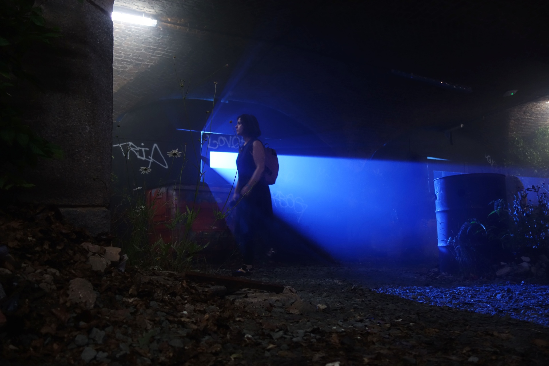 Silhouette walking through blue haze past graffitied walls
