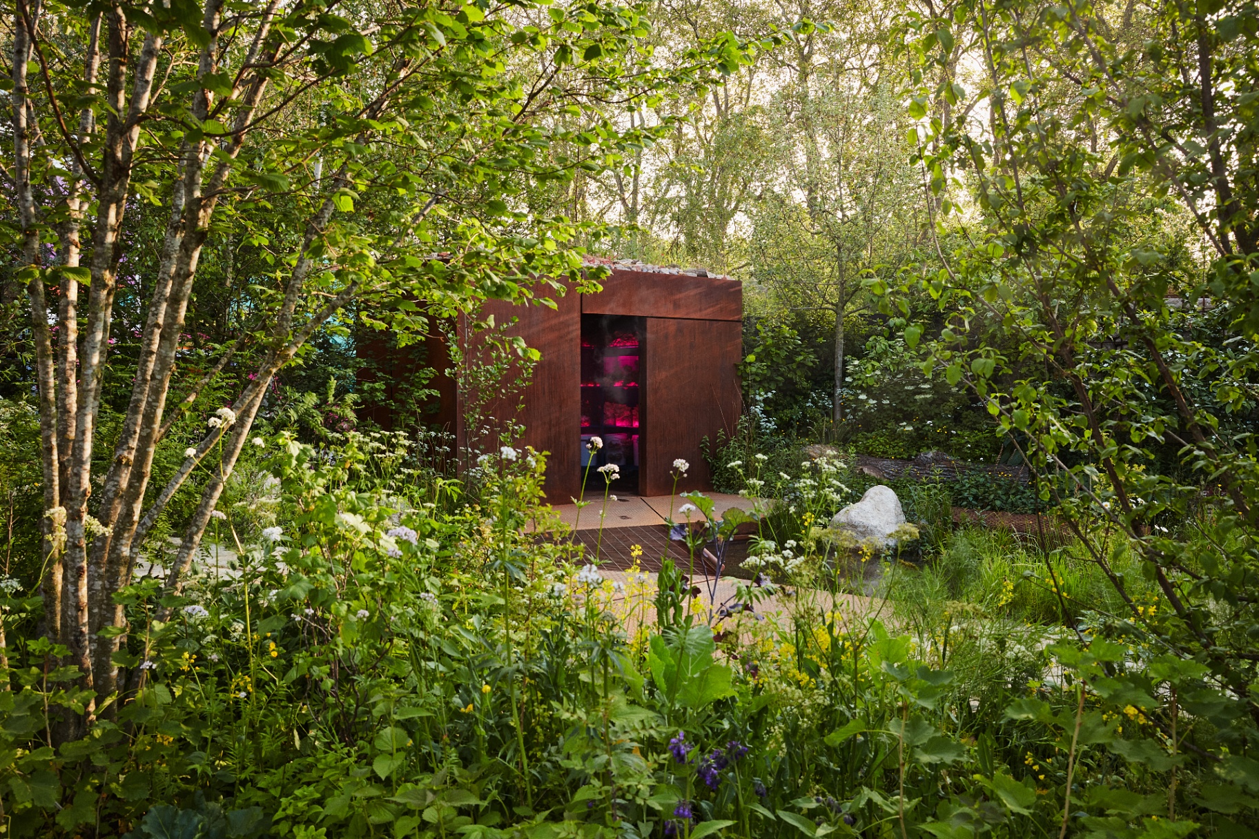 Wide view of the garden with corten shelter nestled among wild planting