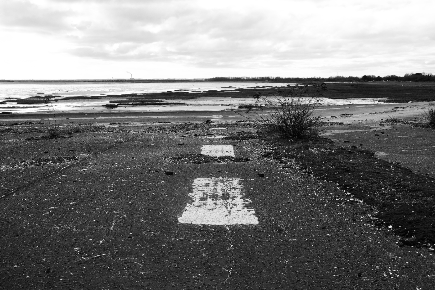 Two faded white rectangles painted on cracked tarmac, leading toward the estuary and distant power station.
