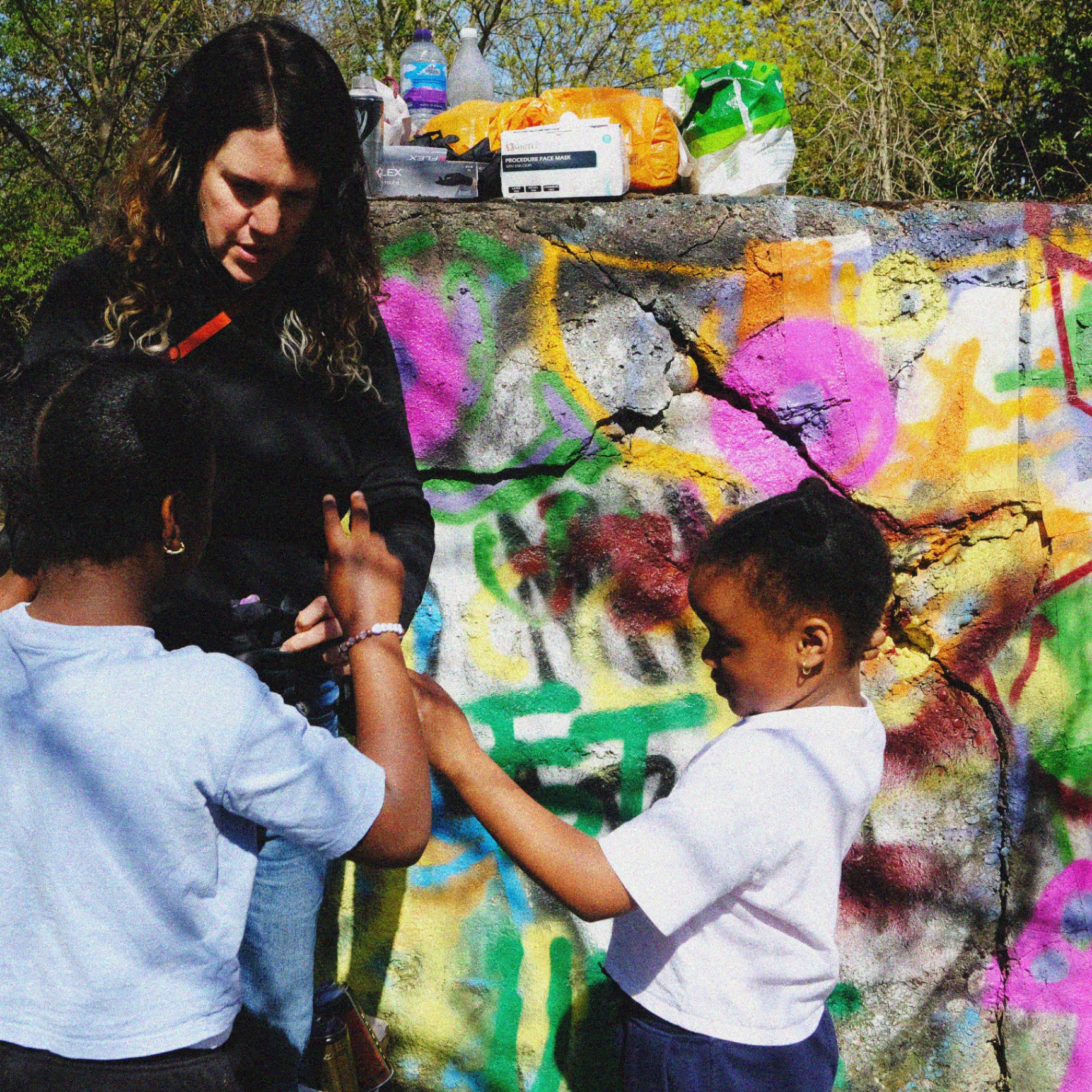 An adult helping two children with spray cans at the mural.