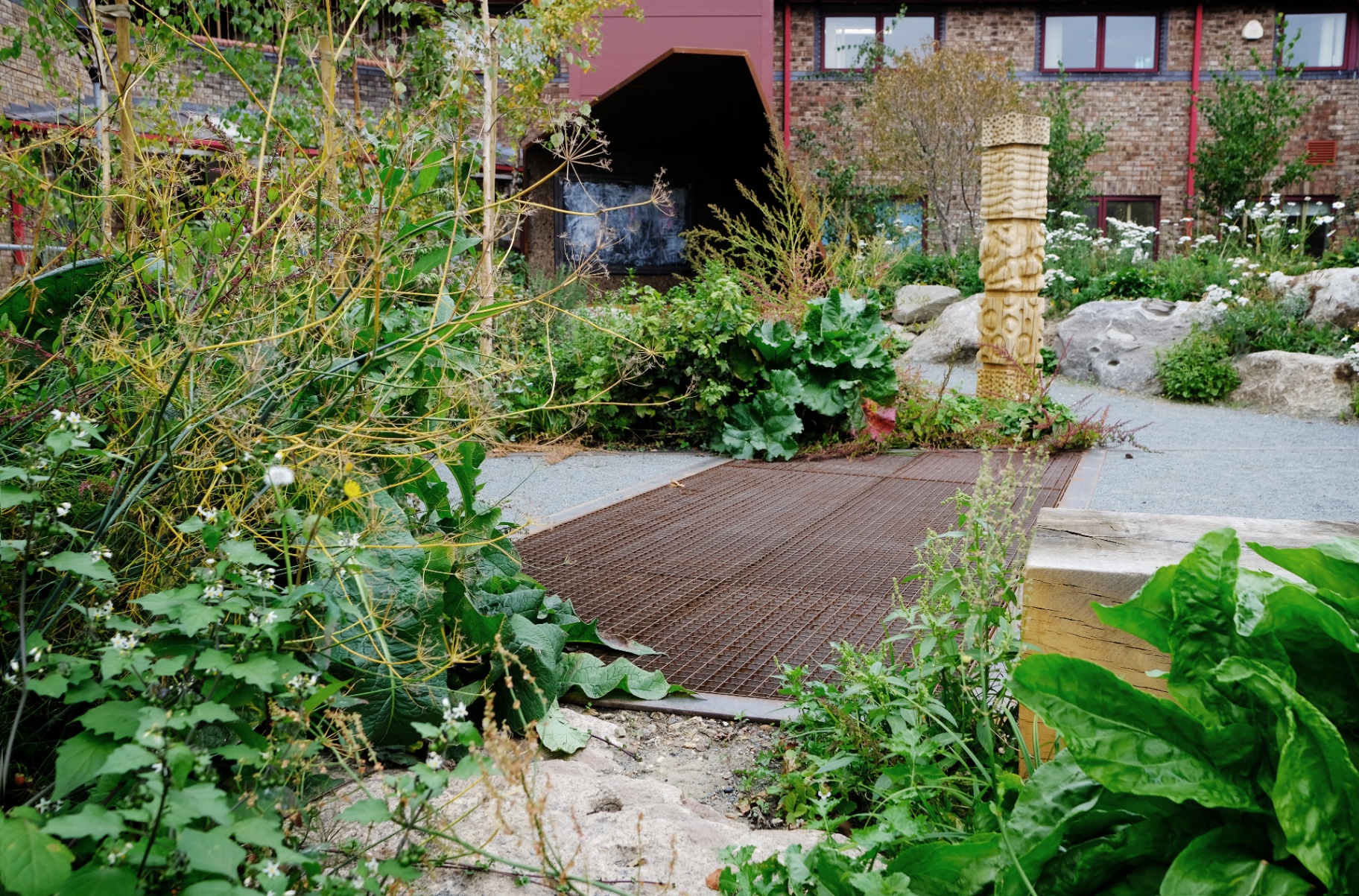 Crush corridor of reused site material between planted beds, carved totem beyond